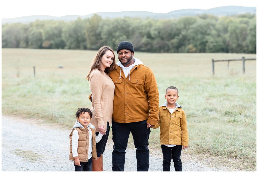 a family of 4 smiles for the camera on a gravel road in a fall family session