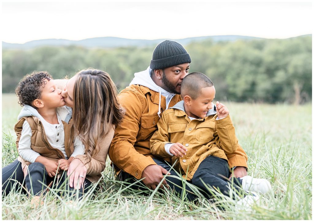 a family of 4 gives each other kisses while sitting on grass at a fall family session