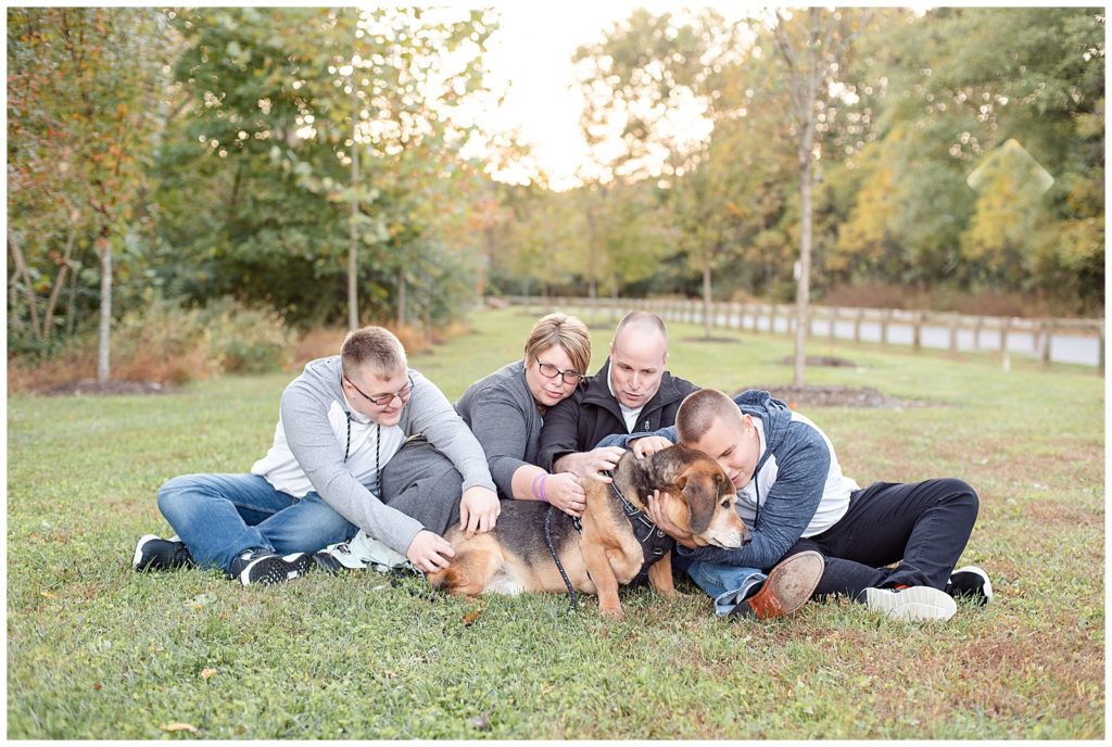 A family of 4 cuddles with their dog at a fall family session