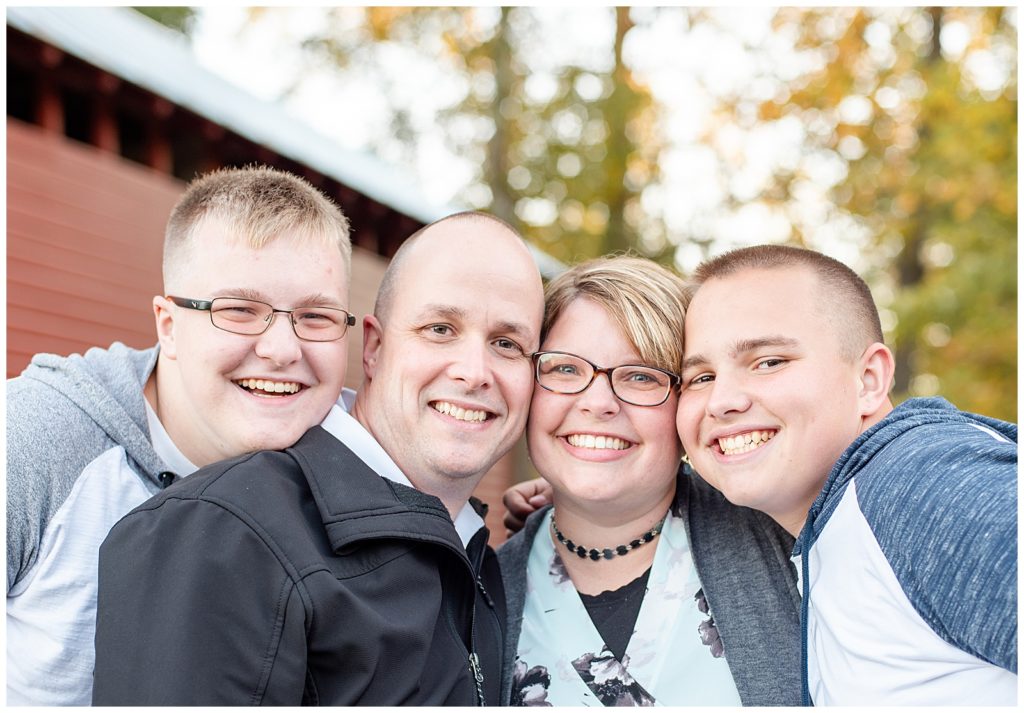 a family of 4 smiles for the camera in front of a covered bridge