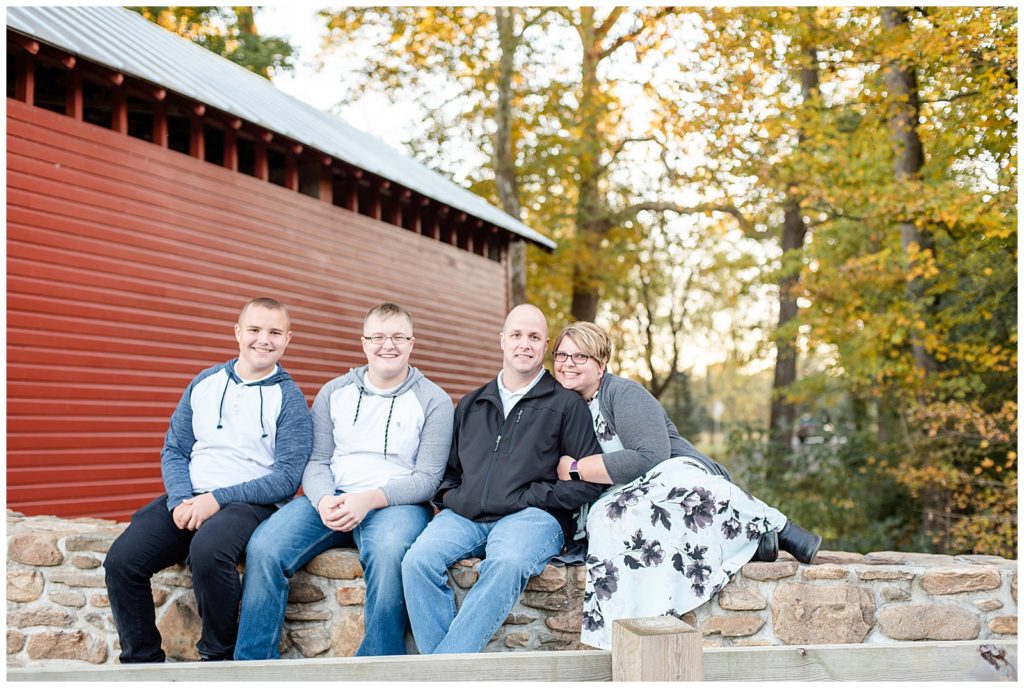 a family sits and smiles in front of a covered bridge