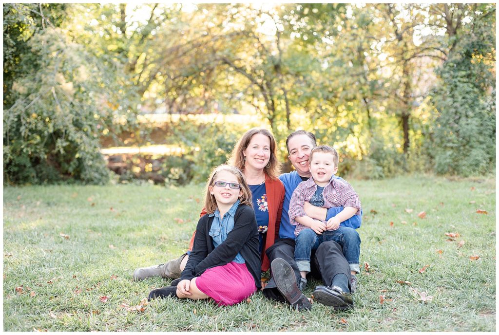 family of 4 sits on the grass and smiles for fall family pictures