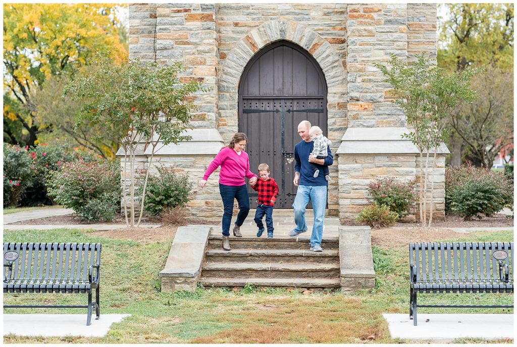 a family of 4 walks down the steps in front of the bell tower