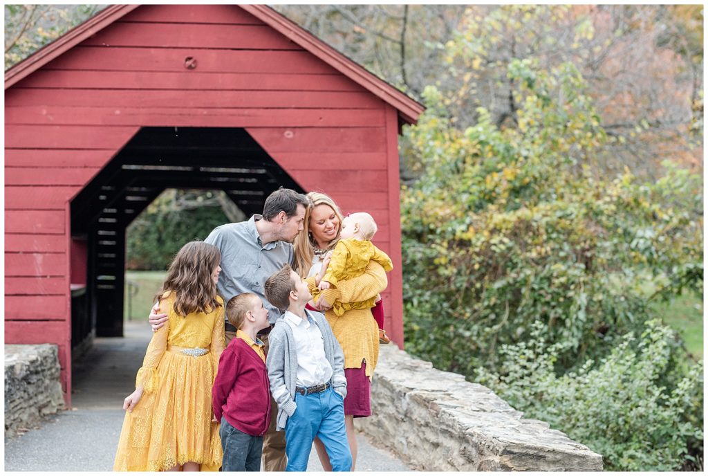a family of 6 play with each other in front of a covered bridge at baker park