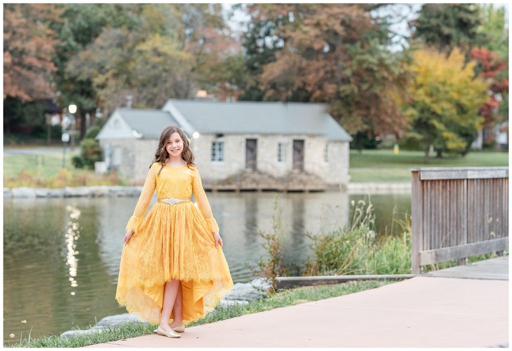 a girl in a yellow dress poses in front of the lake at baker park